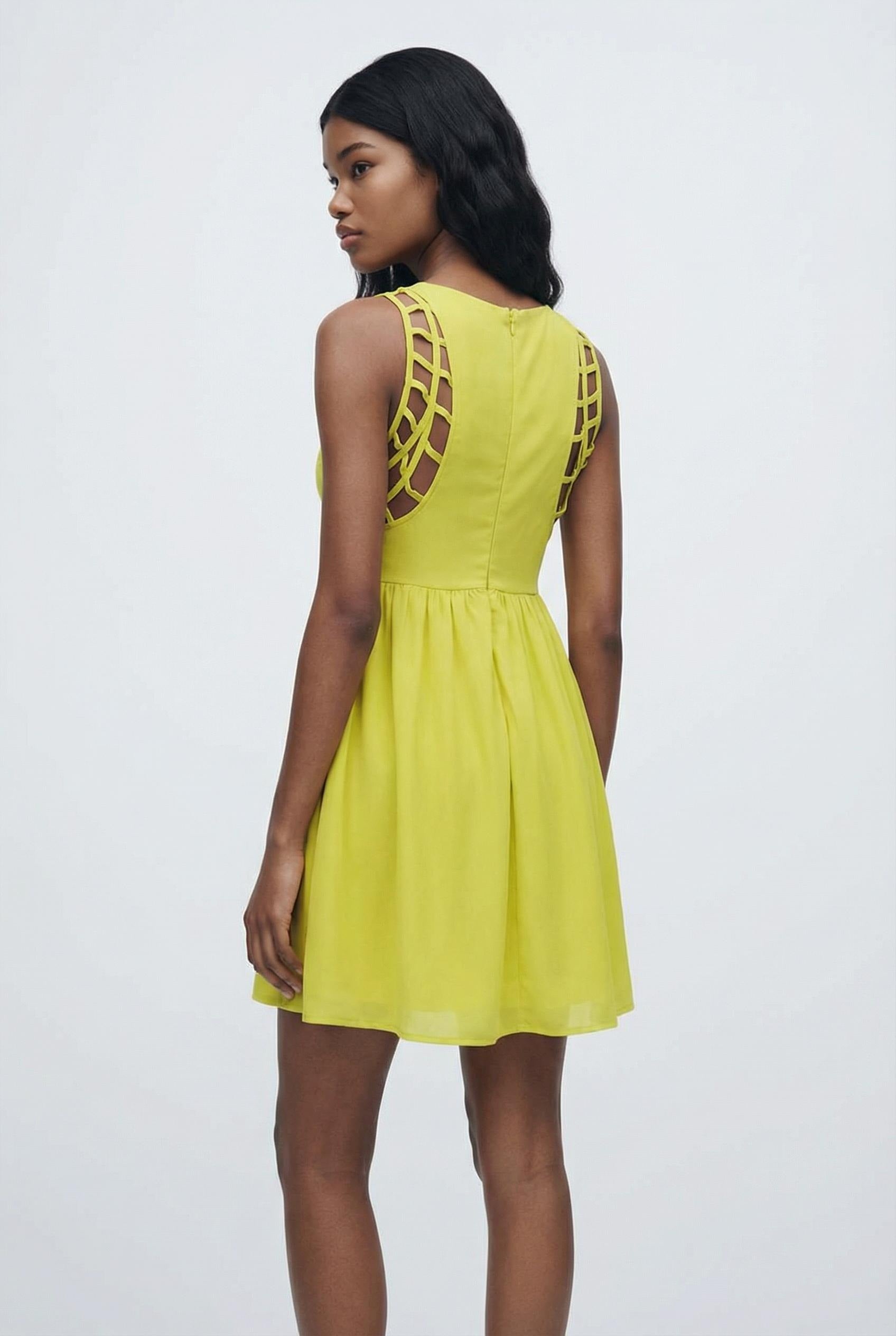 Woman wearing a yellow dress with cut-out shoulders against a white background