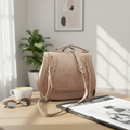 Beige handbag on a table with a magazine underneath against a black background