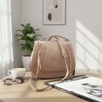 Beige handbag on a table with a magazine underneath against a black background